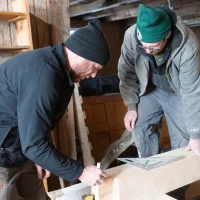Craftsmen marking timber beam for traditional barn restoration