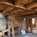 Exposed timber framing and brick chimney inside historic Oakham Massachusetts home during structural restoration
