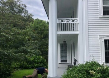 man kneeling near foundation of white house with green lawn