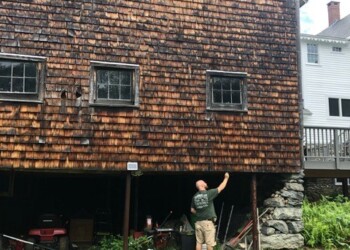 A man standing in front of a wooden building with exposed foundation