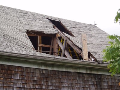 A house with a roof that has giant hole in it exposing wooden beams