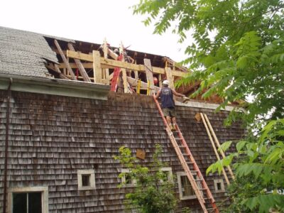 A man on a ladder repairing roof of a house.