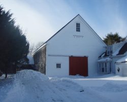 A white barn with a red door in the snow.