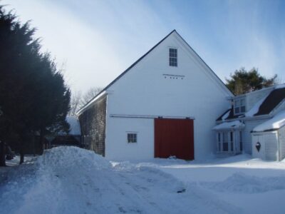 A white barn with a red door in the snow.