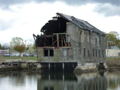 An abandoned house sits on the edge of a body of water.
