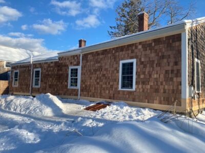 A house in the snow with a shingled roof.