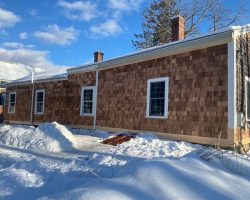 A house in the snow with a shingled roof.